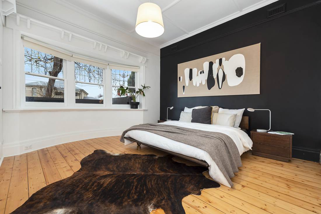 Main bedroom with black feature wall, curved bay of leadlight windows and timber floors