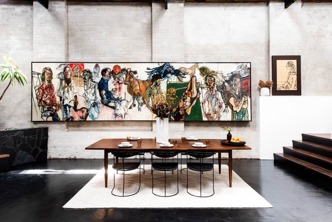 Dining table before a full-width expressionist mural on bagged brick walls