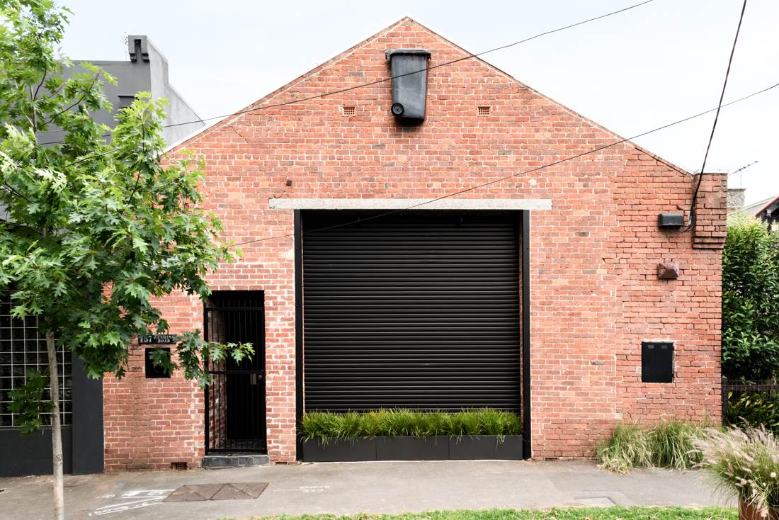 Red brick warehouse facade with black roller door and native grasses