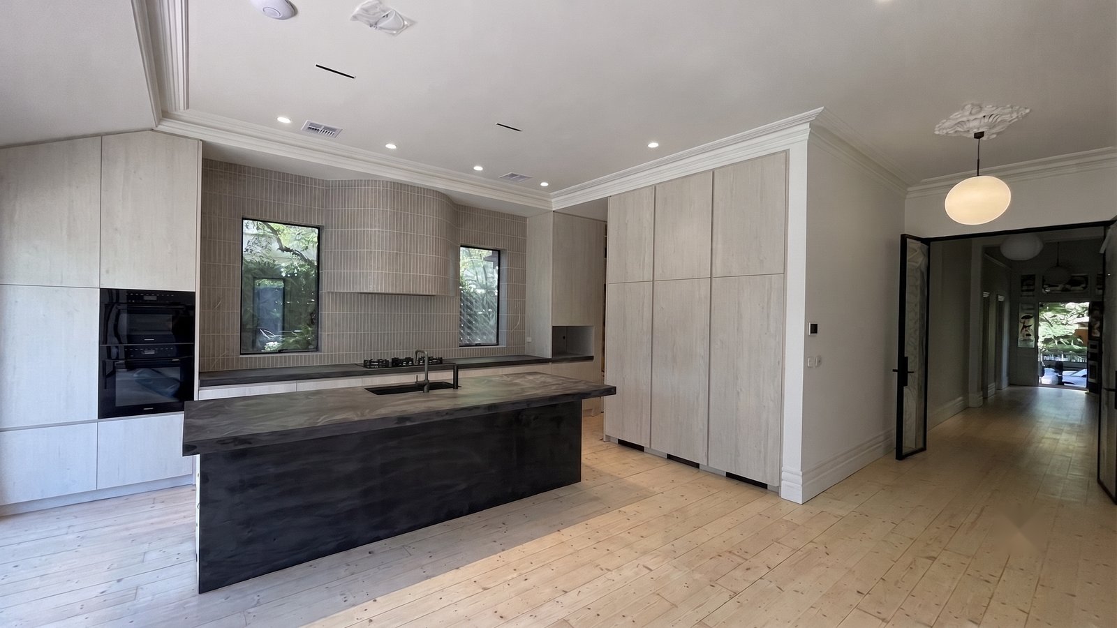 The new kitchen in full — grey-washed timber cabinetry, sage stone benchtops, aged brass hardware and the curved fluted-tile rangehood