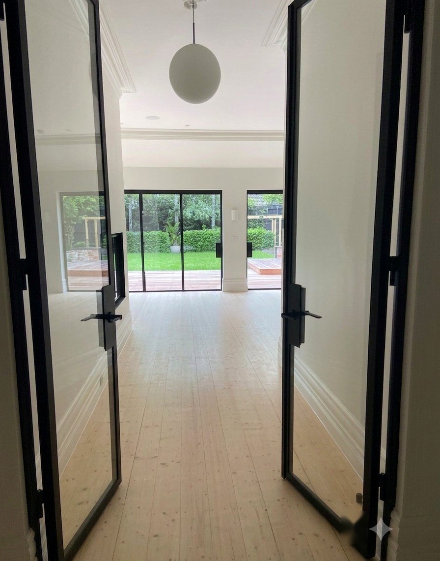 Black steel-framed glass doors at the end of the hallway, opening to the garden