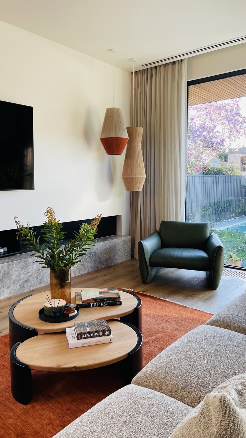The casual living room — green leather Jardan armchair by the glass, Pop and Scott pendants, magnolia in bloom beyond