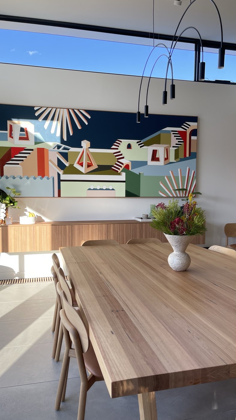 The dining room — a commissioned Jasmine Mansbridge artwork above the credenza, timber table beneath arc pendants and the highline of sky