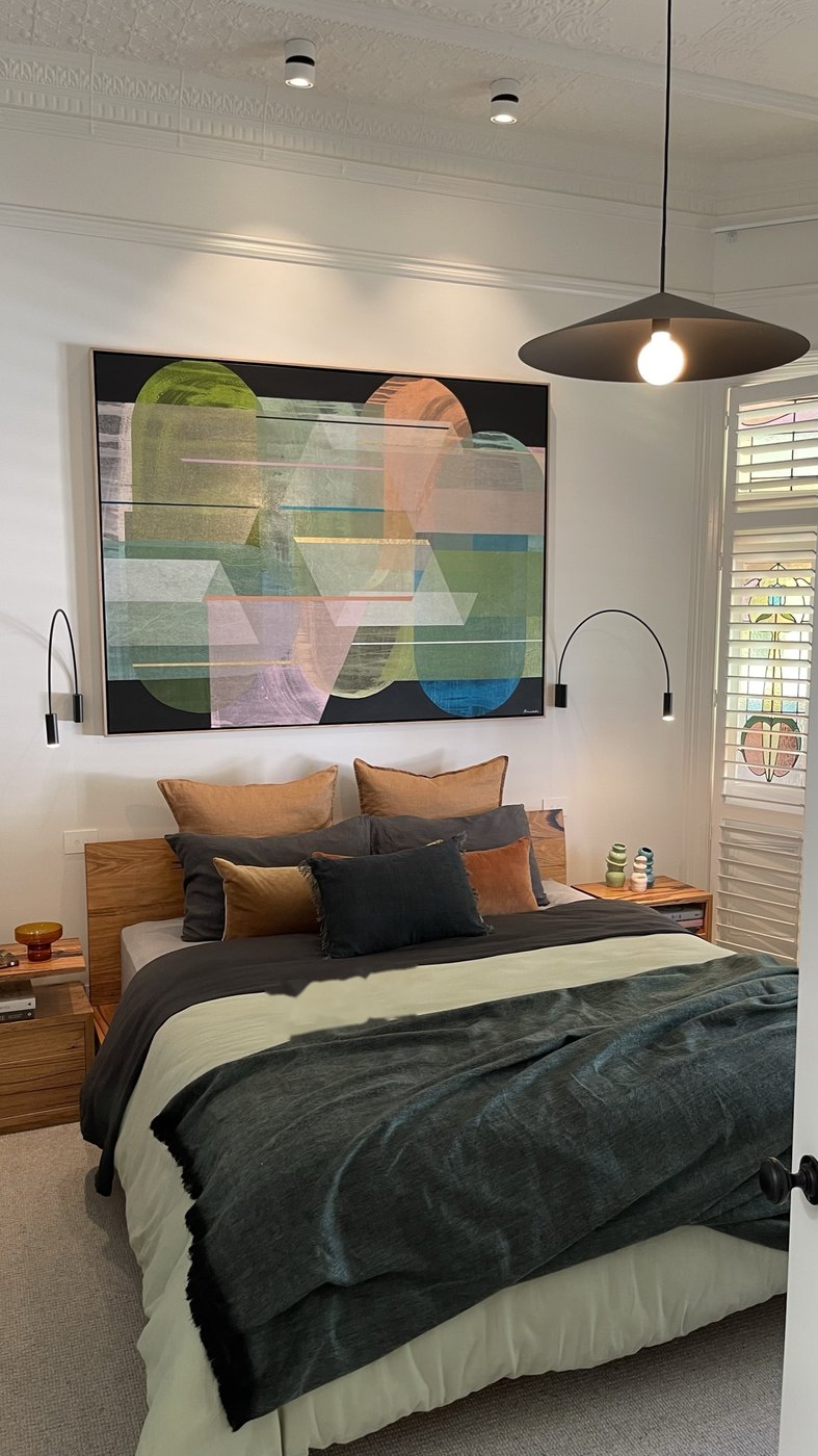 The main bedroom in full — the commissioned Antoinette Ferwerda centred above the bed, arc lights either side, stained glass glowing through the shutters at right