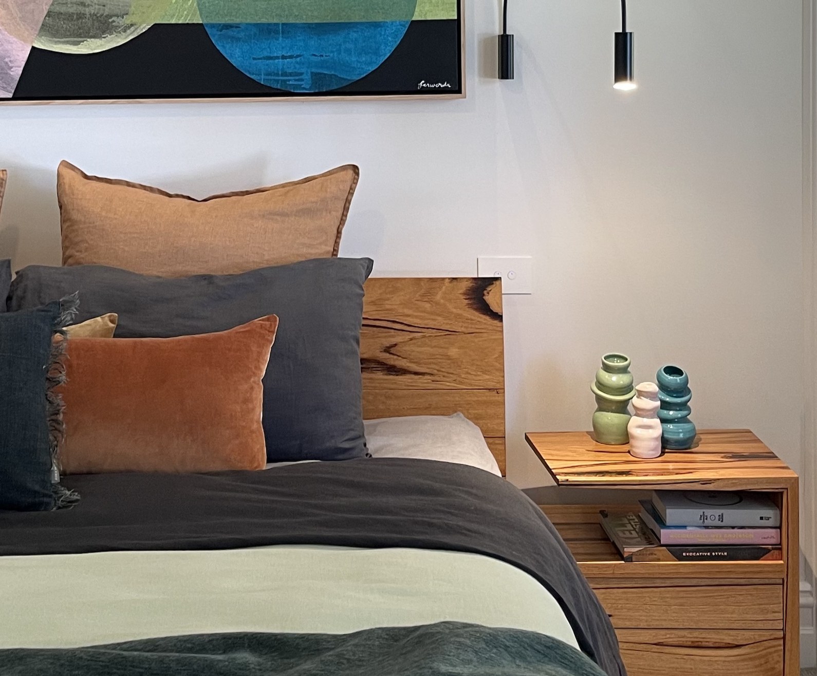 The bedside as a still life — a trio of hand-built Amy Wale vessels on the timber side table, books below, the signed corner of the Ferwerda above
