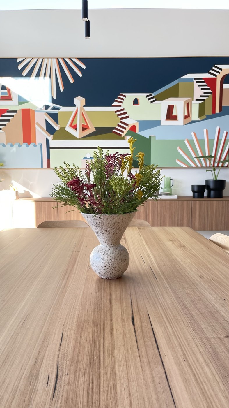 A speckled hand-built Amy Wale vase of native flowers on the dining table, the commissioned Jasmine Mansbridge behind