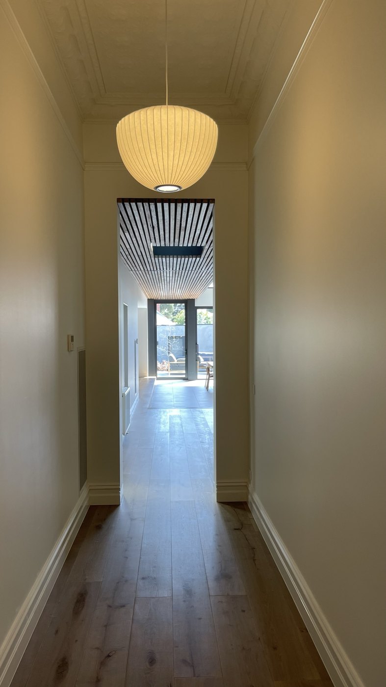 The original hallway restored — pressed ceiling and pendant — opening into the new battened-ceiling volume beyond