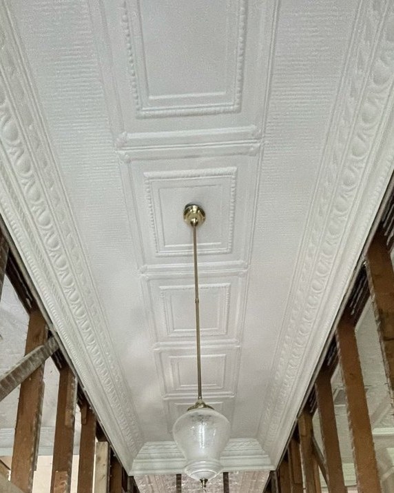 The hallway during works — pressed-metal ceiling and brass pendant intact above the stripped timber frame