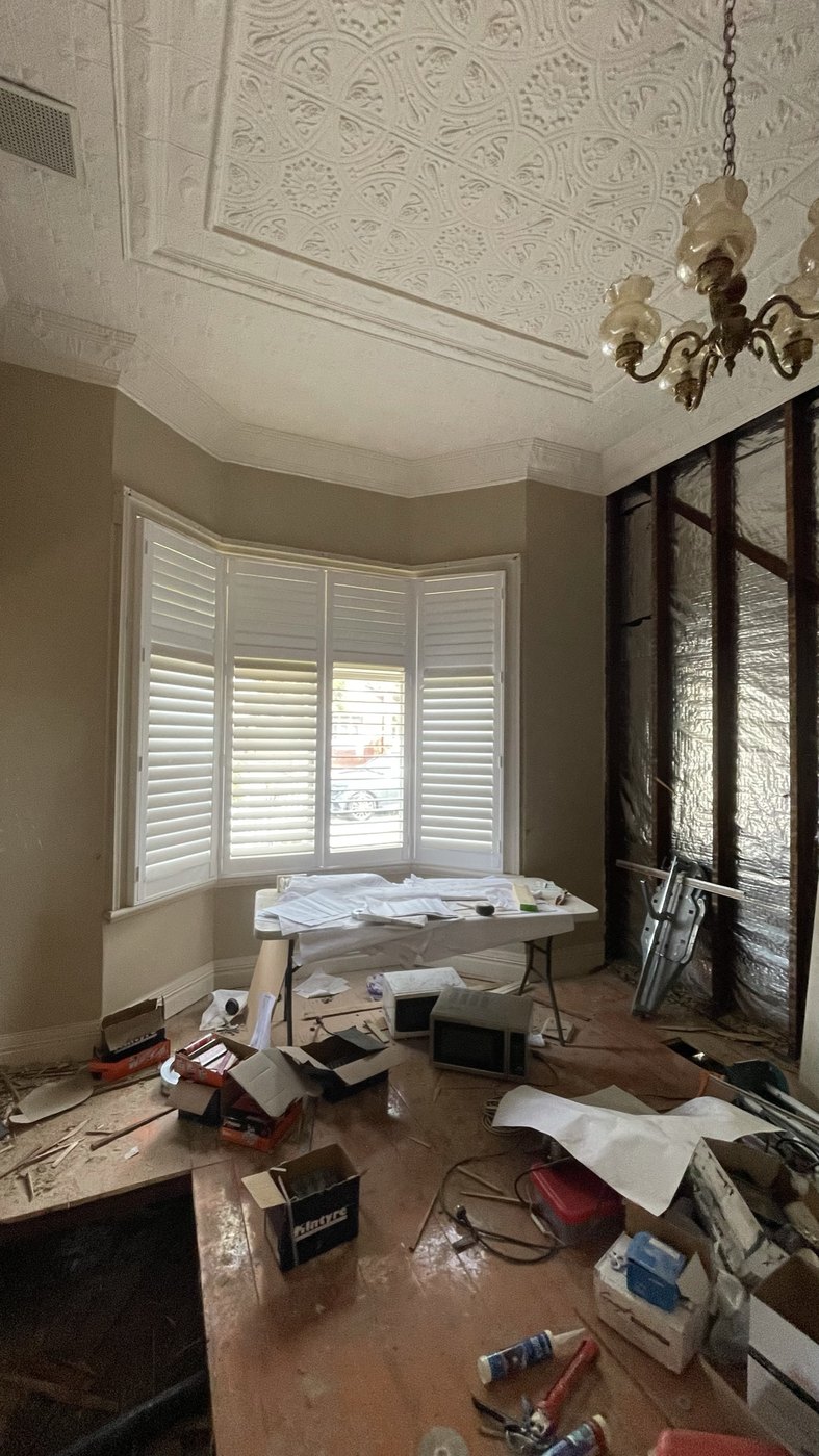 The formal lounge during works — pressed ceiling and chandelier above a stripped room