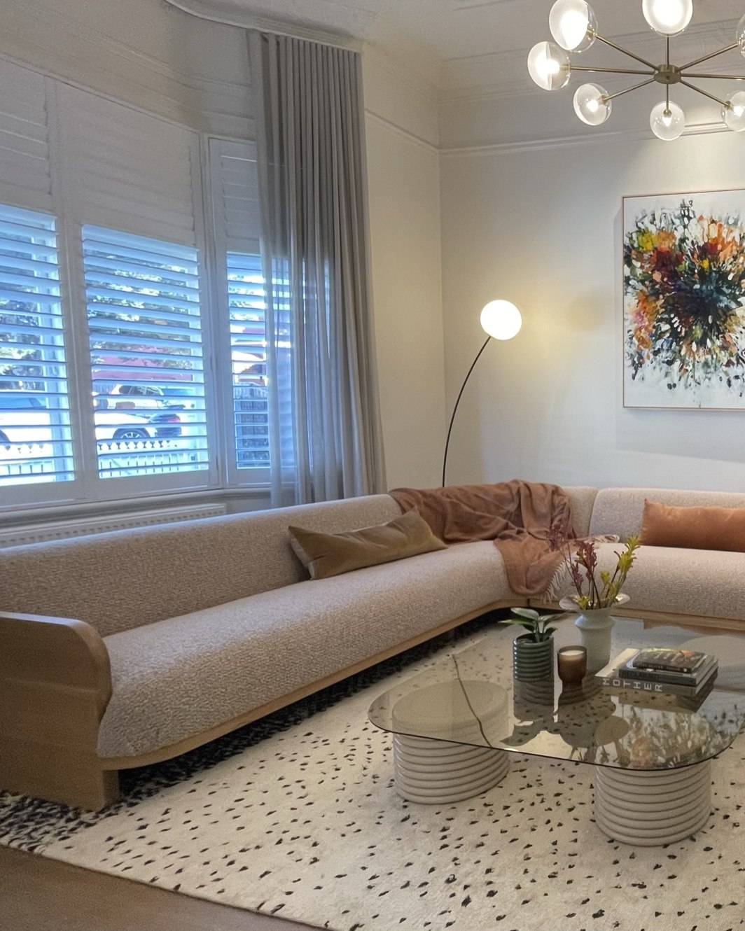 The formal lounge finished — the same bay window and shutters, Jardan sofa wrapping the corner beneath the commissioned Michael Bond