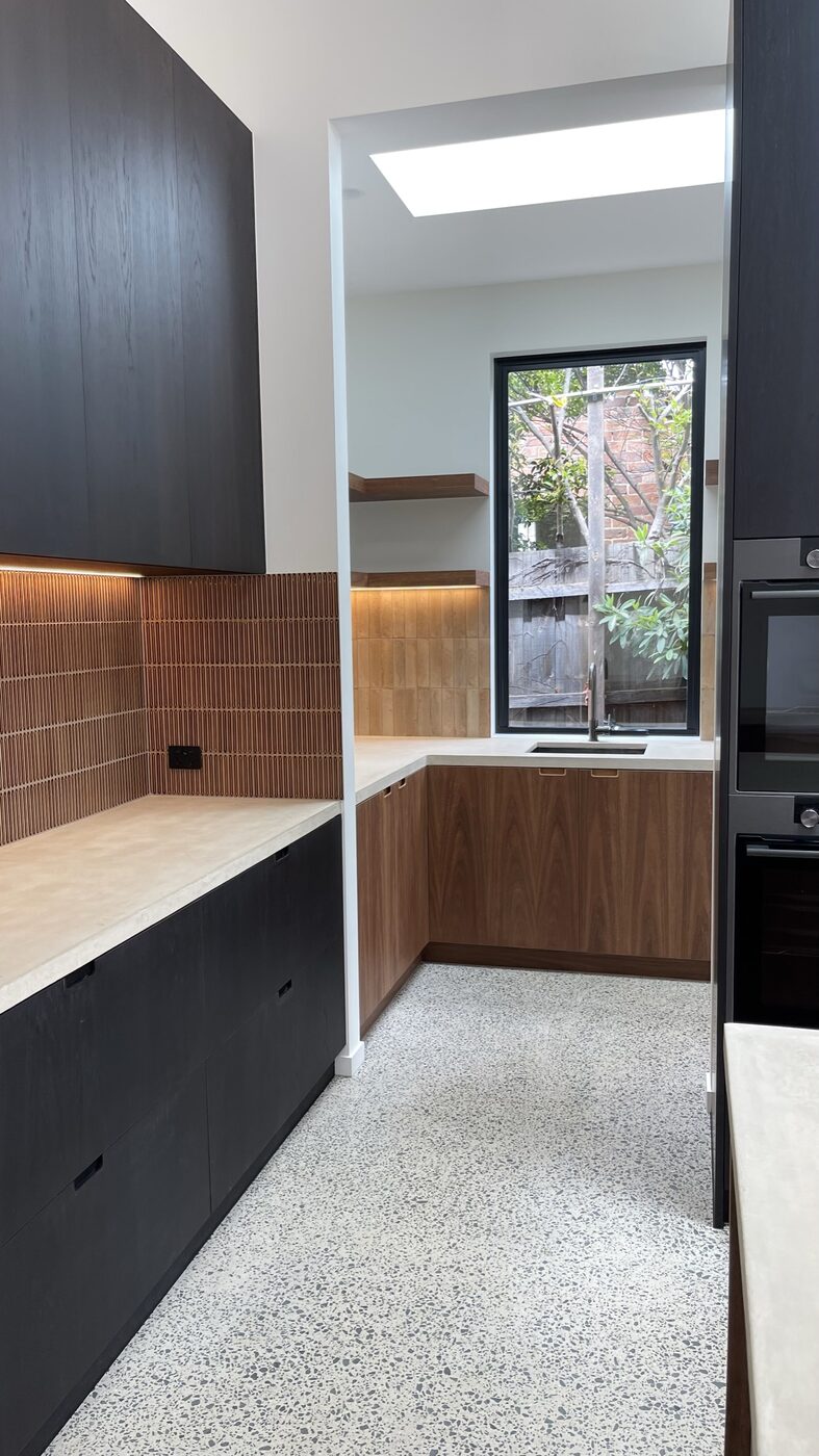 The new kitchen — black-stained oak and spotted gum cabinetry, polished concrete benchtops and a caramel fluted tile splashback, looking through to the butler's pantry under a skylight