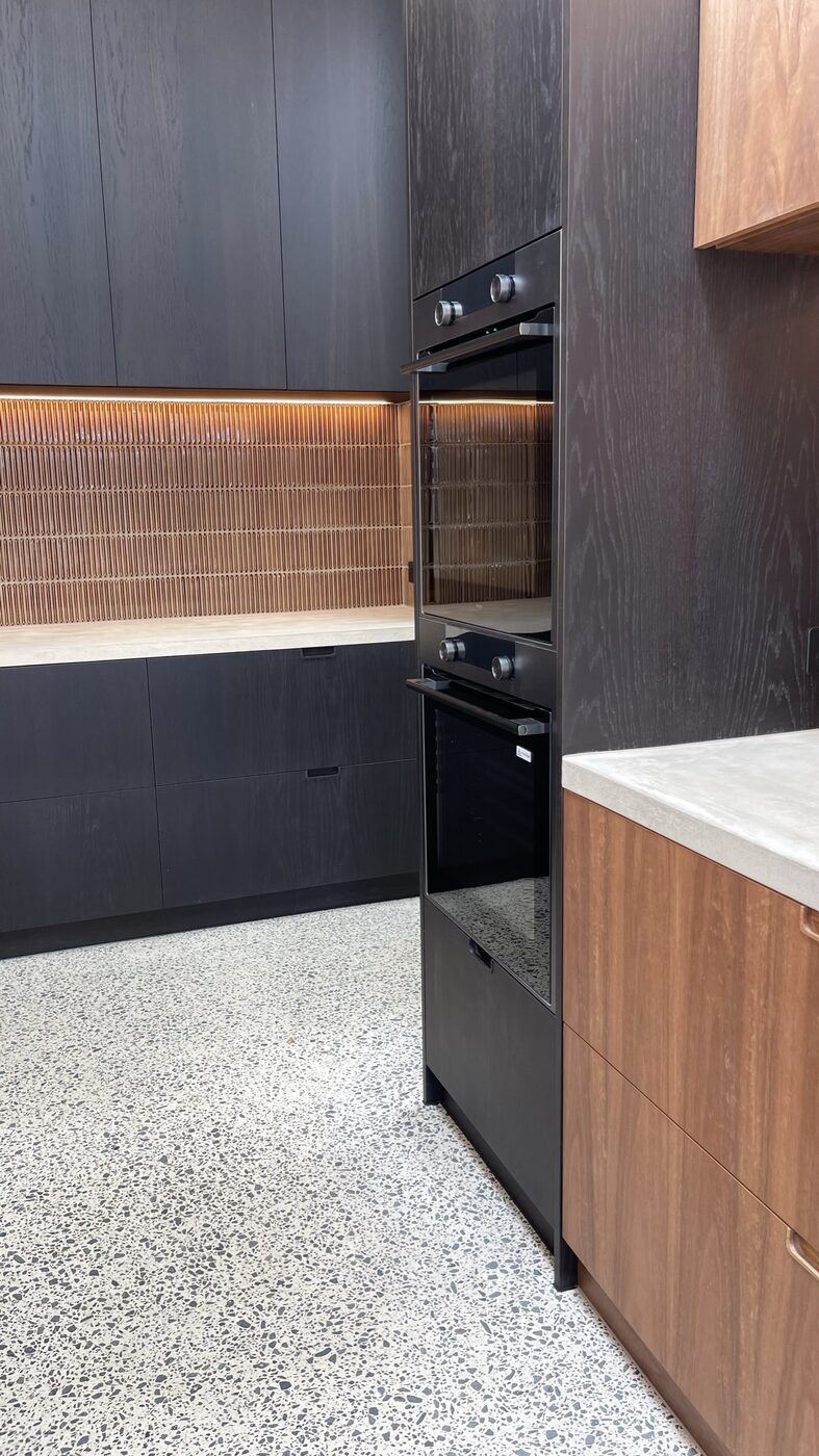 The oven tower in black-stained oak, the fluted caramel tile lit from above