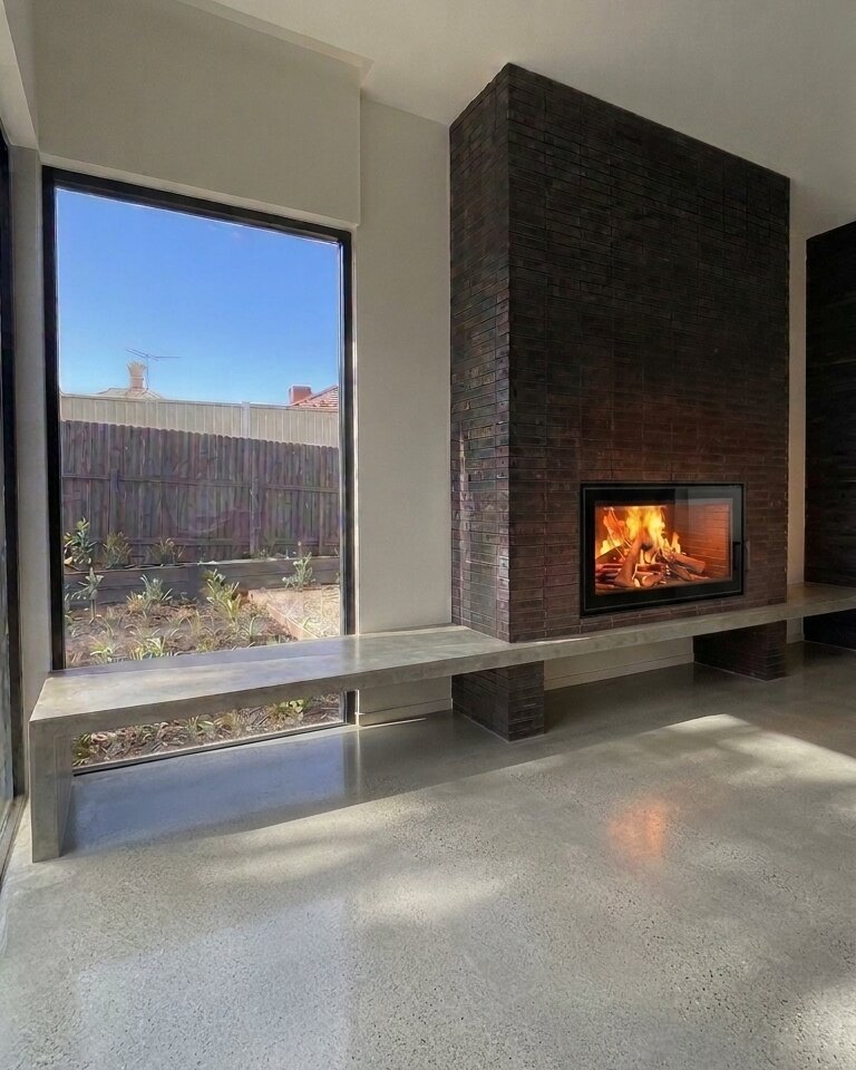 The new fireplace — dark brick chimney with an inbuilt wood fire and a long cast concrete hearth floating past the garden window