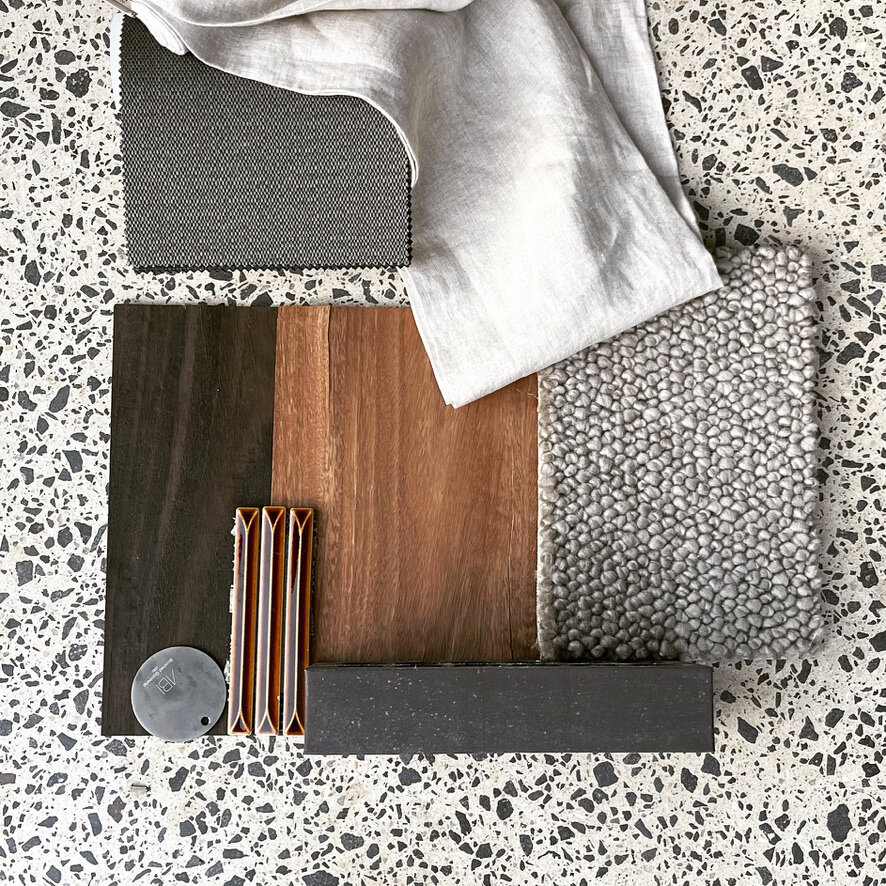 The Waverley material palette laid out on the polished concrete floor — spotted gum, black-stained oak, fluted caramel tiles, brushed gunmetal, linen and bouclé