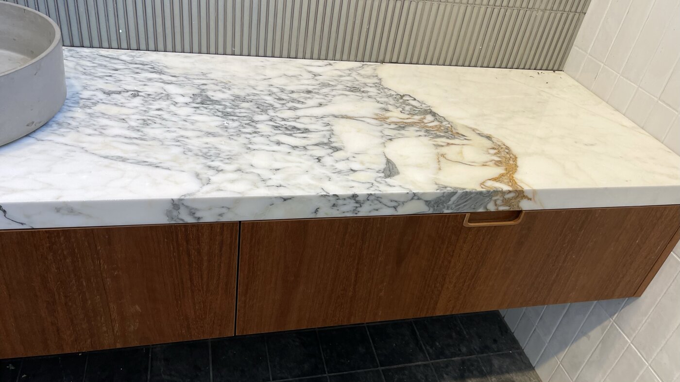 The ensuite vanity — a gold-and-grey veined marble slab over spotted gum drawers with recessed timber pulls