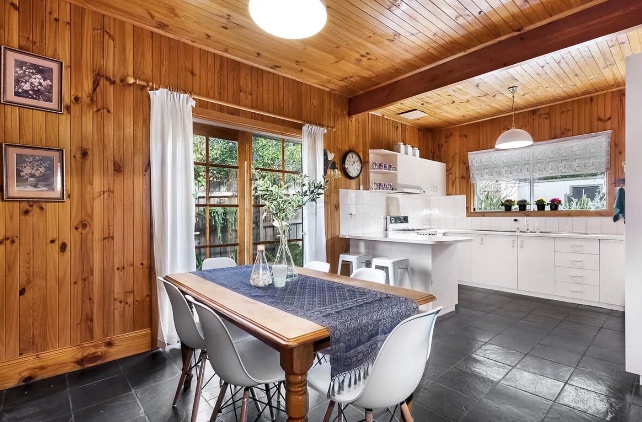 The original kitchen and dining — pine-lined walls and ceiling, dark slate floor, a small white peninsula kitchen